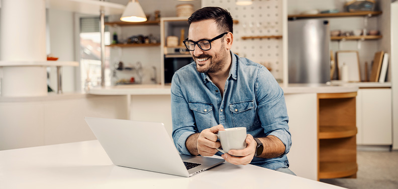 homem sorrindo e tomando café enquanto lê seus e-mails em um notebook