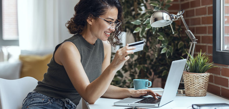 mulher segurando um cartão de crétido e fazendo compra online no computador