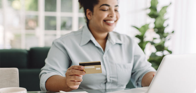 mulher segurando um cartão de crédito, usando um notebook para fazer o cadastro em um clube de assinatura
